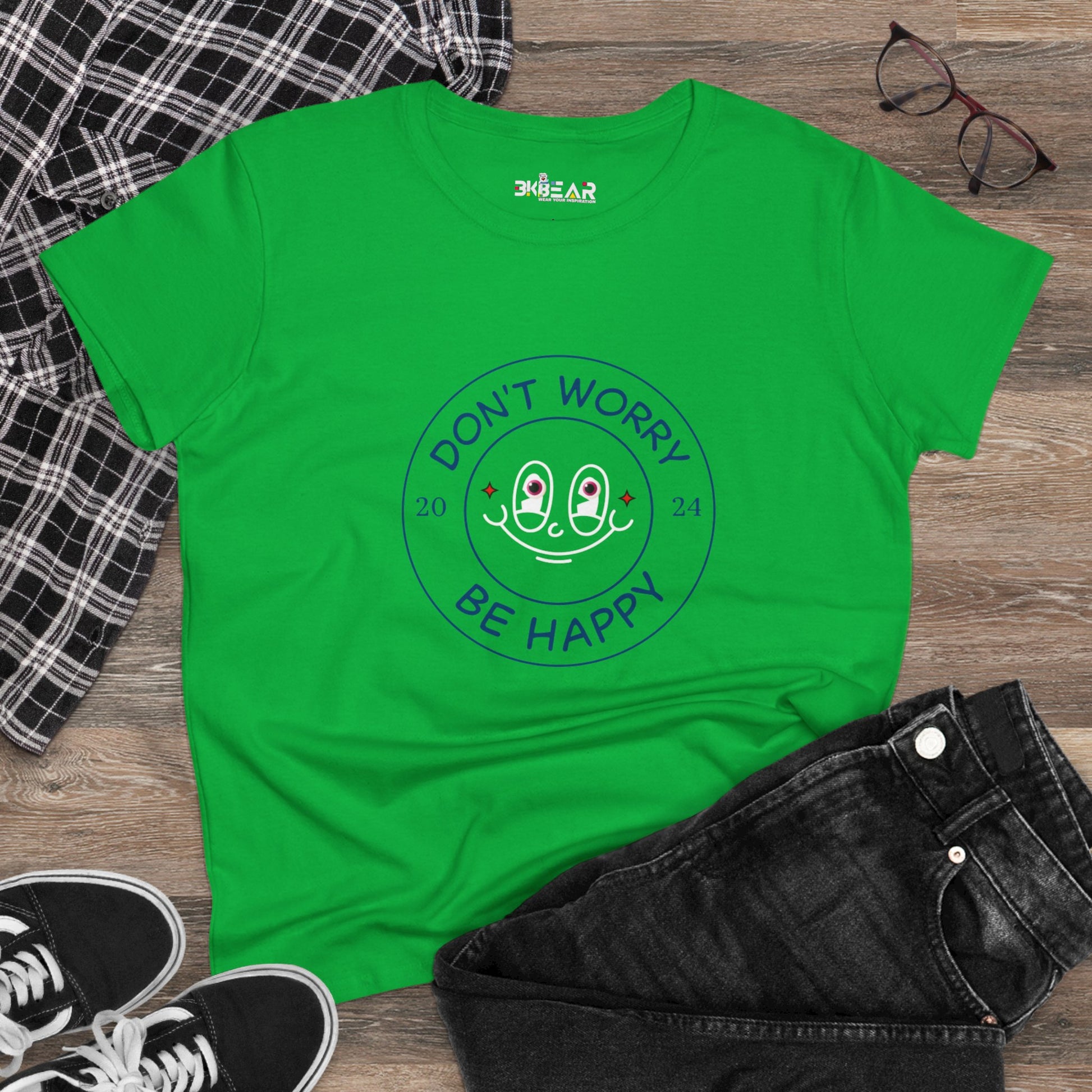 Green Printify don’t worry be happy t-shirt with a smiling face graphic laid out with black jeans and sneakers