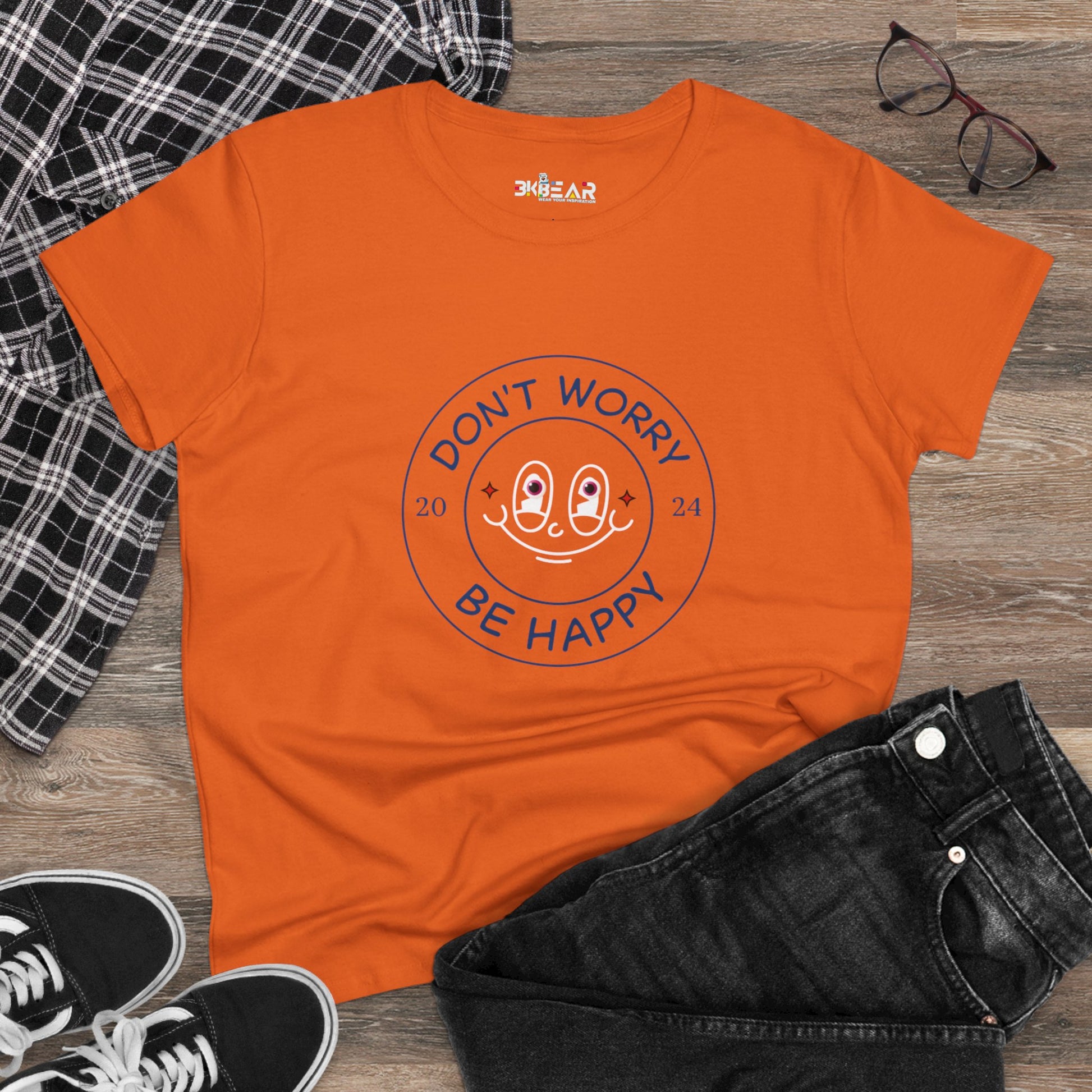 Orange Printify don’t worry be happy t-shirt with smiley face graphic laid flat with black jeans and sneakers