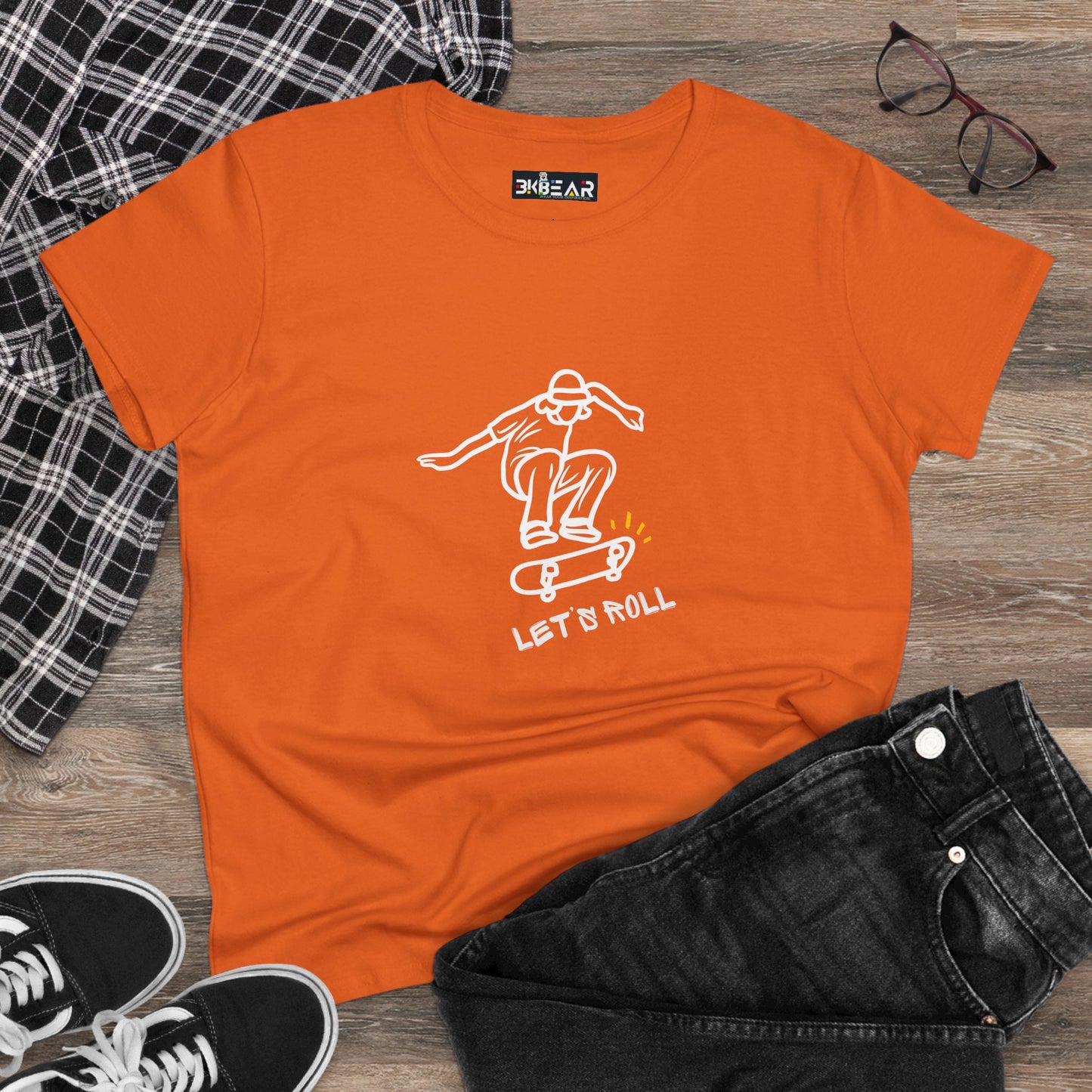 Orange Let’s Roll shirt with skateboard graphic, laid flat with black jeans and plaid shirt