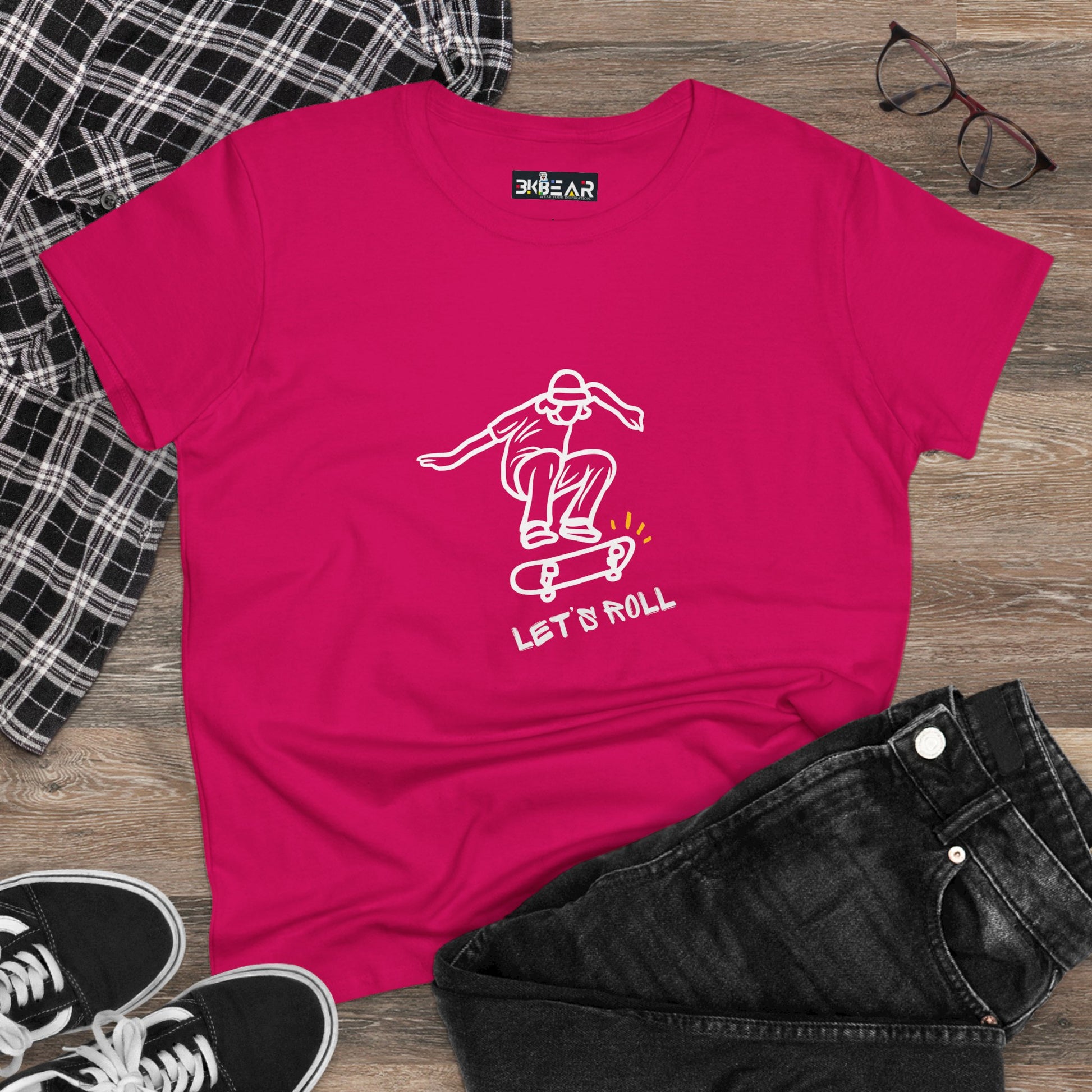 Bright pink Let’s Roll shirt with a white skateboarder graphic, styled with black jeans and sneakers