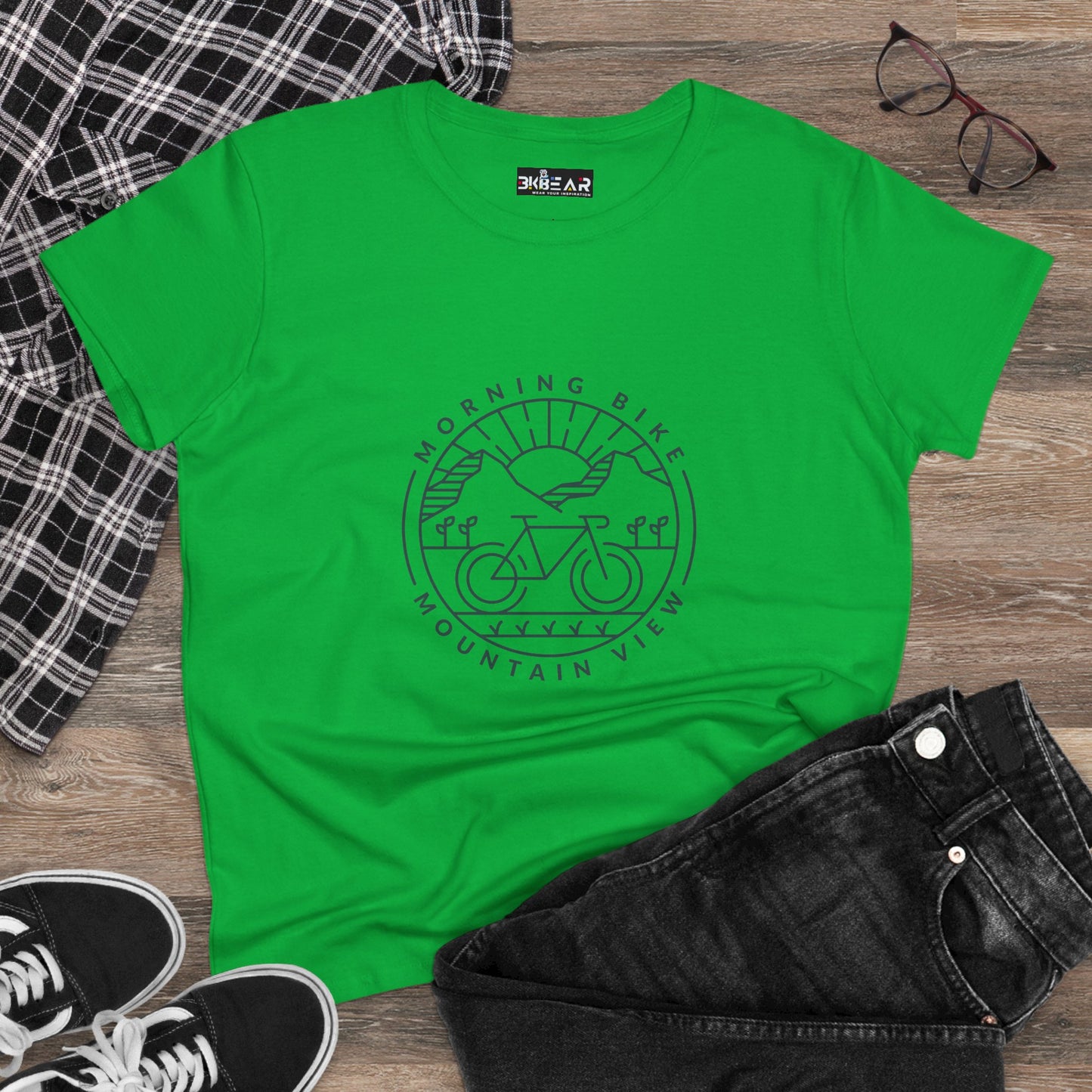 Green morning bike t-shirt with mountain and bike graphic laid out with black jeans and checkered shirt