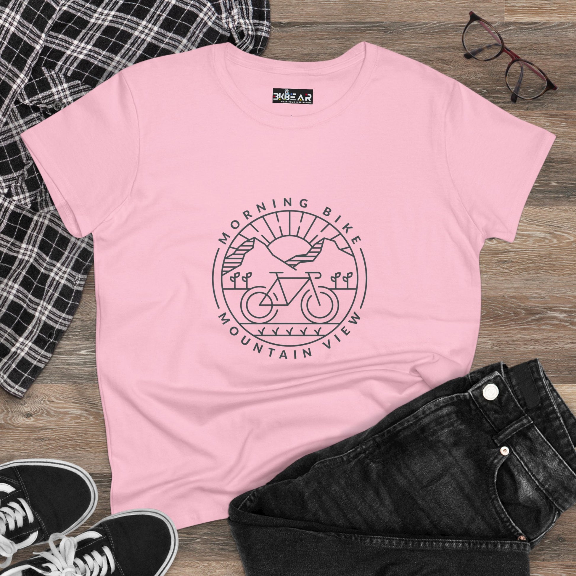 Pink morning bike t-shirt with mountain and sunrise graphic laid out with black jeans and sneakers