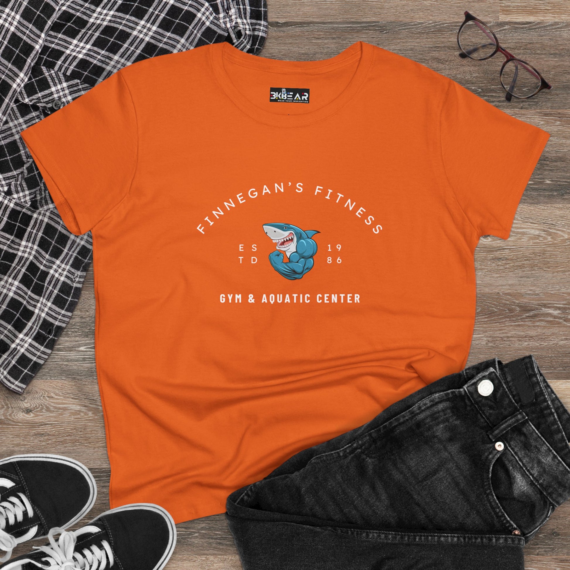 Orange workout shirt women graphic with Finnegan's Fitness shark logo and Gym & Aquatic Center text