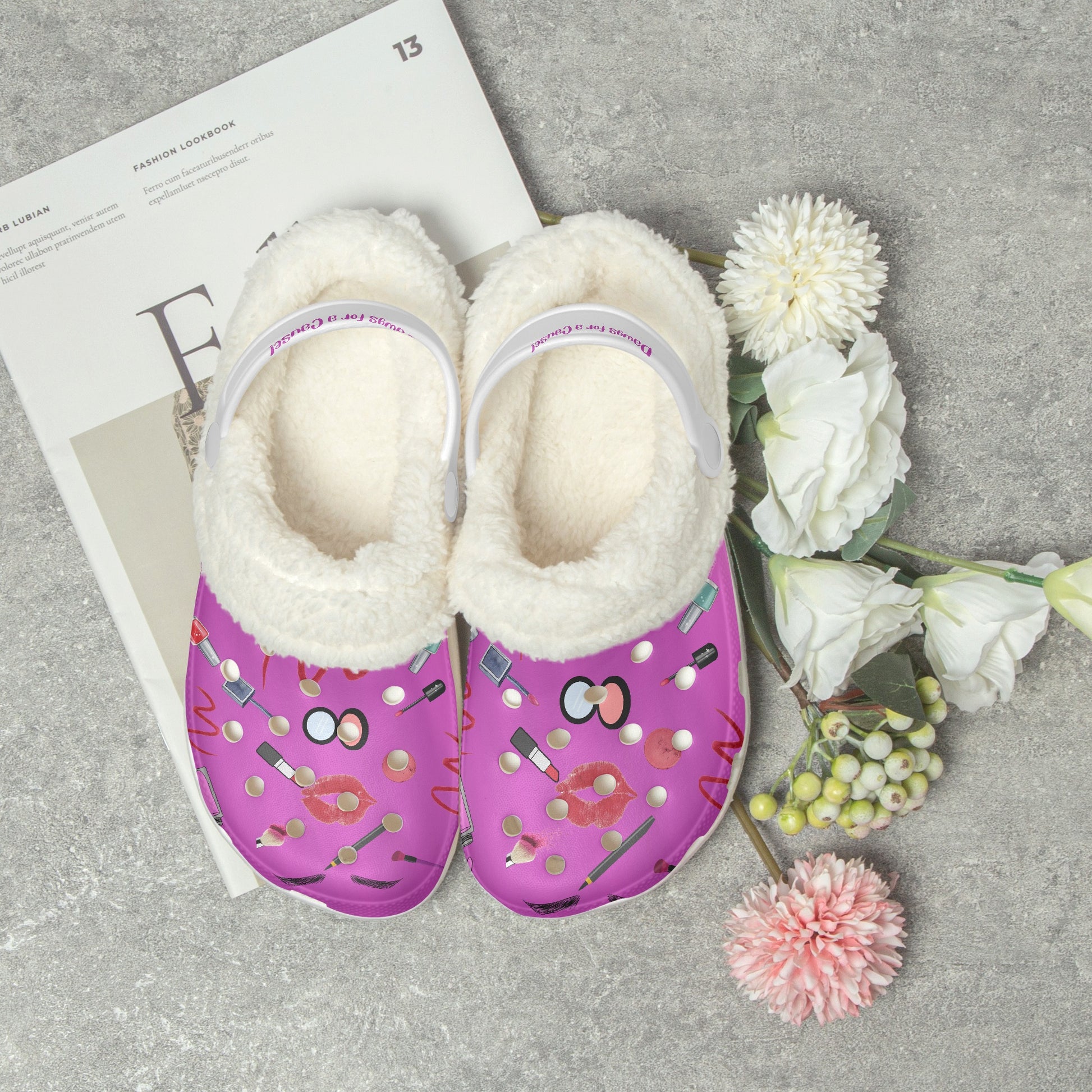 Pink fuzzy clogs for women with white fluffy lining and playful makeup print on gray surface