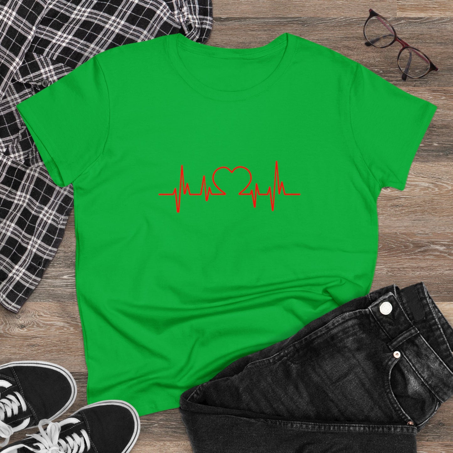 Green heartbeat graphic t-shirt with red heart and pulse line design laid flat with black jeans and sneakers