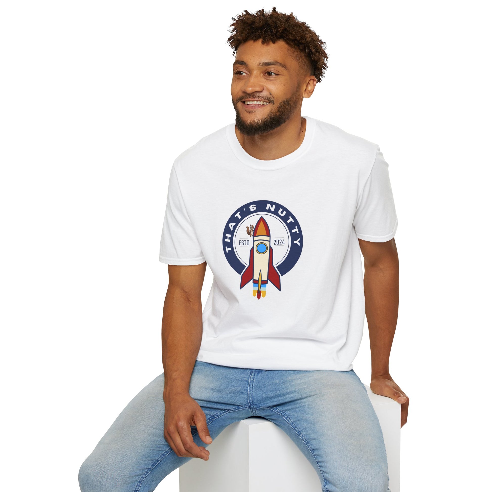 White Printify t-shirt with rocket ship tee graphic worn by smiling man sitting on white block