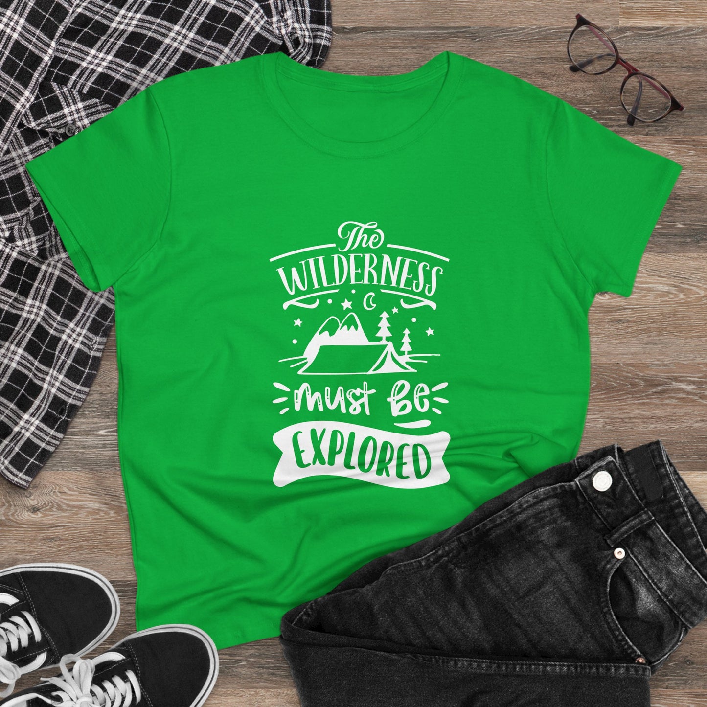 Green wilderness exploration shirt with white adventure graphic laid out with black jeans and sneakers